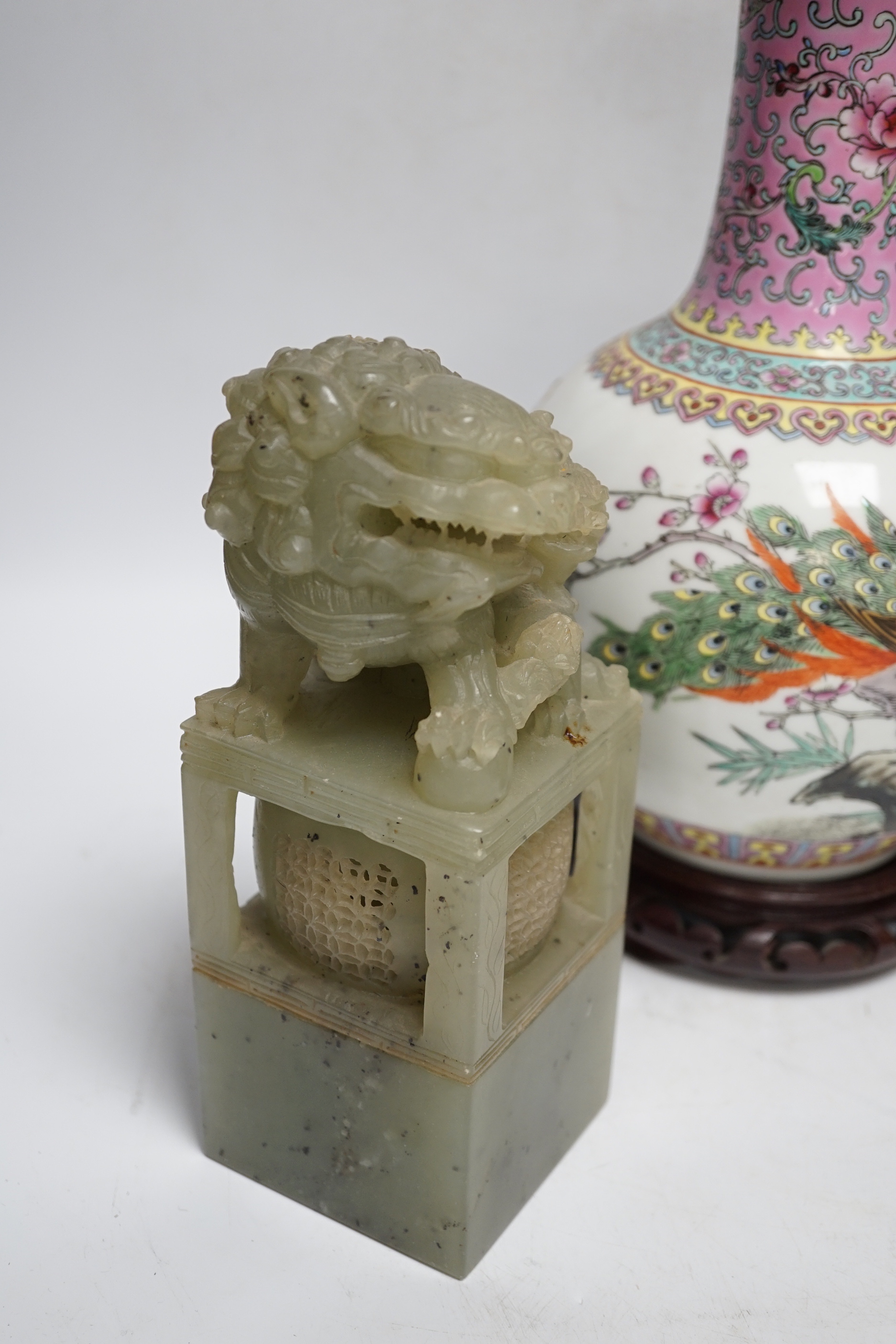 A pair of large Chinese soapstone ‘Temple Guardian lion’ seals, 21cm, and a Chinese famille rose vase, 27cm, on carved wood stand